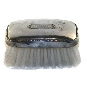 May include: A silver-plated hair brush with a rectangular lid. The lid has an engraved inscription that reads "Ruby".
