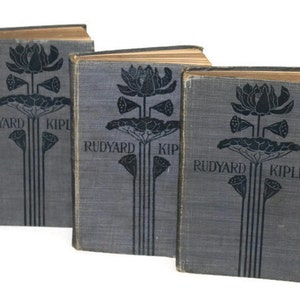 May include: A set of three vintage hardback books by Rudyard Kipling with a decorative floral design on the cover. The books are bound in a dark gray fabric with black lettering and illustrations.