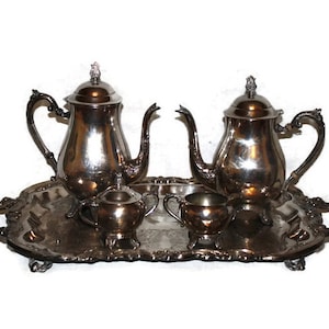 May include: A silver tea set with two teapots, a creamer, and a sugar bowl, all on a silver tray with ornate handles.