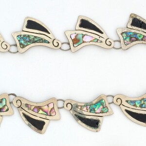 May include: A silver necklace with black and iridescent abalone shell accents. The necklace is made of a chain with a series of pendant-like pieces that are shaped like a stylized wing.