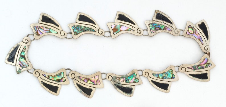 May include: A silver necklace with black and iridescent abalone shell accents. The necklace is made of a chain with a series of pendant-like pieces that are shaped like a stylized wing.