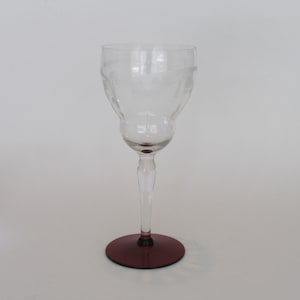 May include: A clear glass wine glass with a cut design and a burgundy colored base.