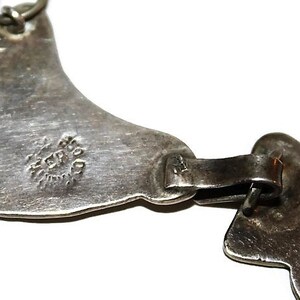 May include: A silver necklace with a unique design featuring two connected crescent shapes. The necklace has a hallmark that reads "STERLING".