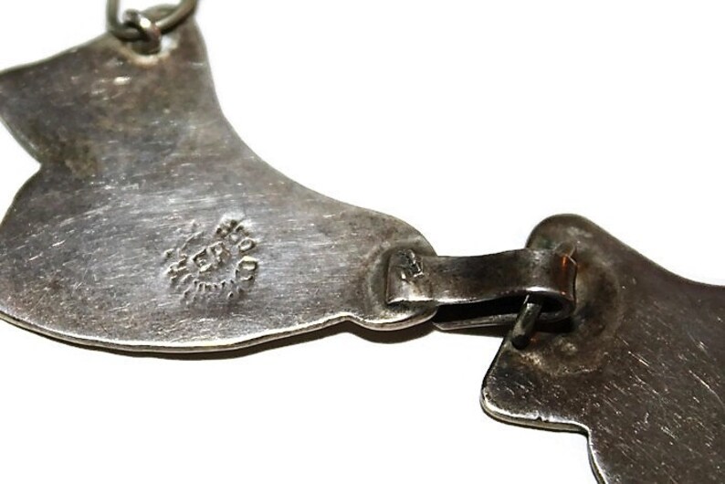 May include: A silver necklace with a unique design featuring two connected crescent shapes. The necklace has a hallmark that reads "STERLING".