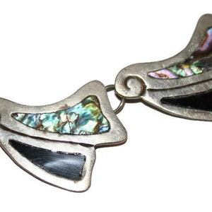 May include: A silver necklace with a geometric design featuring abalone shell and black accents. The necklace is made of multiple pieces that are connected together.