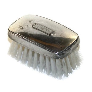 May include: A silver-plated brush with a white bristle brush. The brush has an engraved design and the name "Hill" is engraved on the top.