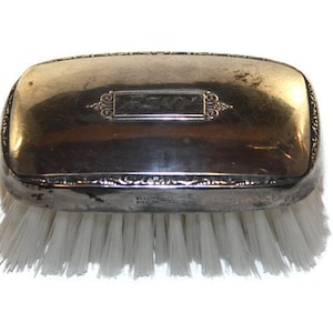 May include: A silver-plated brush with white bristles. The top of the brush has an engraved inscription.