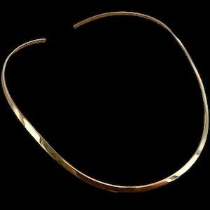 Może przedstawiać: Złoty naszyjnik typu choker o prostym, eleganckim designie. Naszyjnik ma gładki, zakrzywiony kształt i polerowane wykończenie. Końce naszyjnika mają wzór tekstury. Tło jest czarne.