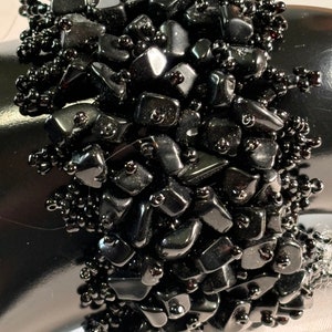 May include: A black beaded bracelet with black gemstone chips. The bracelet is made with small black beads and larger, irregularly shaped black gemstone chips.