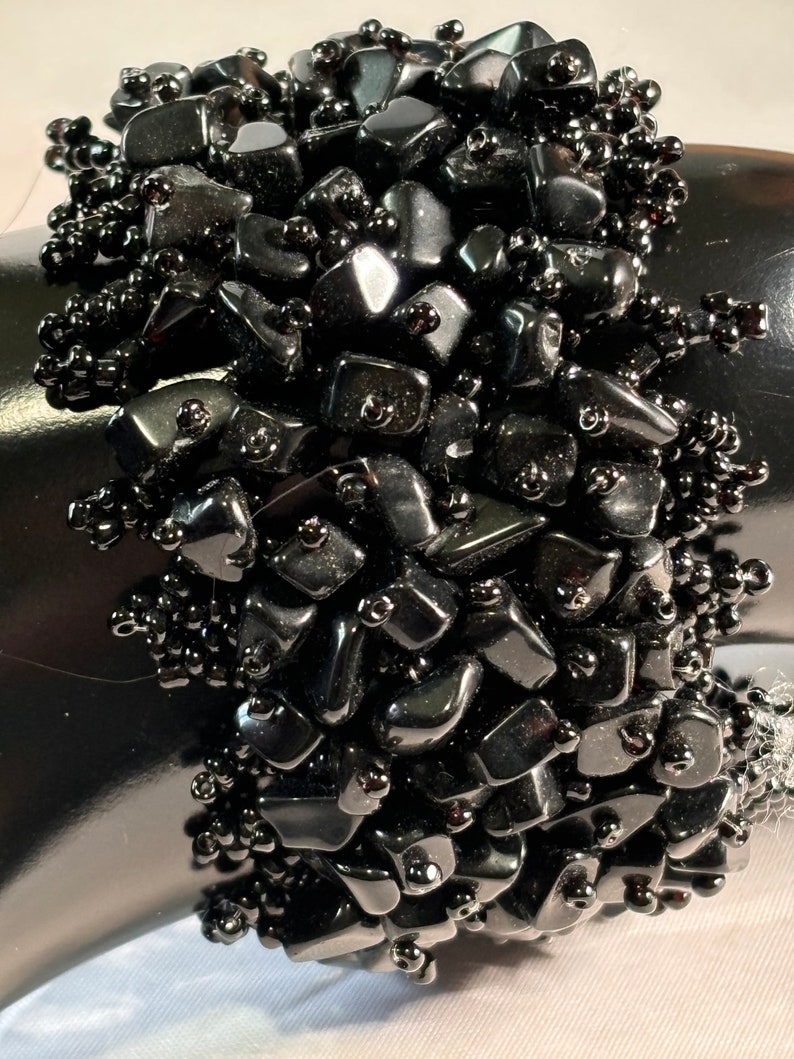 May include: A black beaded bracelet with black gemstone chips. The bracelet is made with small black beads and larger, irregularly shaped black gemstone chips.