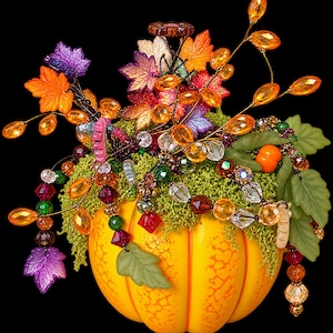 May include: A yellow pumpkin base topped with green moss and an arrangement of colorful acrylic leaves in orange, purple, and red. The display features dangling strands of faceted crystal beads in amber, green, and clear tones, accented with small green leaves.