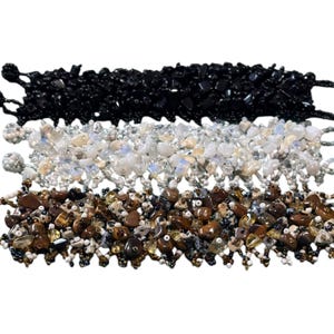 May include: Three beaded bracelets with different colored stones. The top bracelet has black stones, the middle bracelet has white stones, and the bottom bracelet has brown and gold stones.
