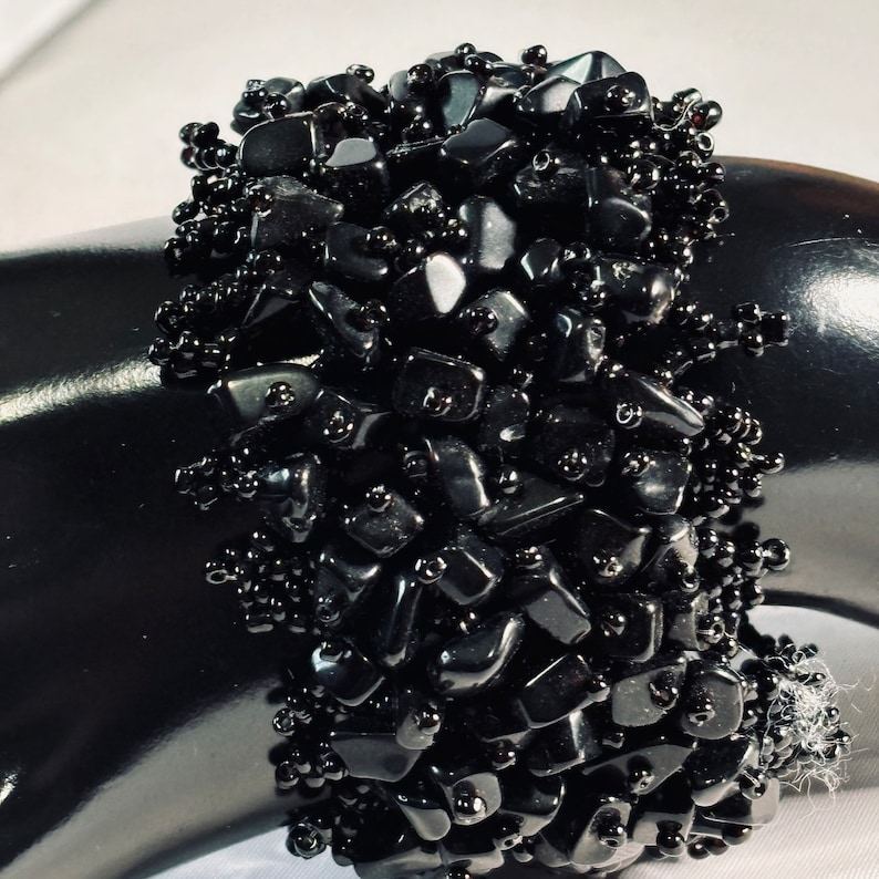 May include: A black beaded bracelet with black gemstone chips. The bracelet is made of small, irregular shaped black stones and black beads.