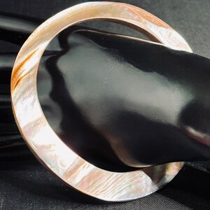 May include: A large, round, iridescent, mother-of-pearl bangle bracelet.