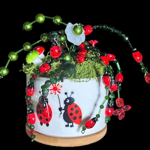 Puede incluir: Una taza de cerámica blanca con un asa negra y el texto "But First, Coffee" en negrita negra. La taza se encuentra sobre un fondo neutro, resaltando su diseño simple.