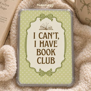 May include: A clear rectangular tablet or e-reader case featuring a light green background with white polka dots. The center displays a cream-colored ornate frame with a bow at the top and bottom, containing the text I CAN'T, I HAVE BOOK CLUB.
