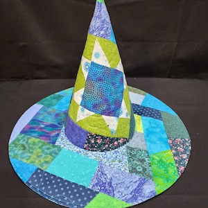 May include: A conical hat constructed from a patchwork of quilted fabric squares in various shades of blue, green, and white. The design features a prominent star pattern on the cone and a wide, flat brim composed of assorted floral and geometric prints.
