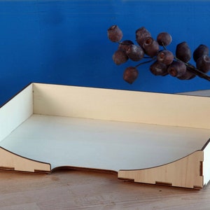 Könnte beinhalten: Ein helles Holztablett mit abgerundeten Kanten und einem weißen Innenraum. Das Tablett ist leer und steht auf einer Holzoberfläche.