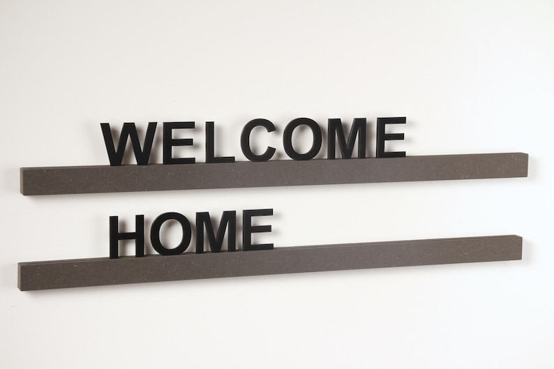 Puede incluir: Dos estantes de madera marr&oacute;n con las palabras "WELCOME" y "HOME" en letras negras.