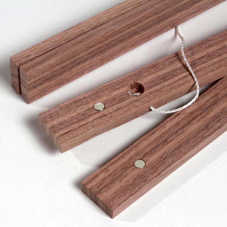 May include: Three wooden dowels with a white string attached to one of them. Each dowel has a small silver magnet embedded in the wood.