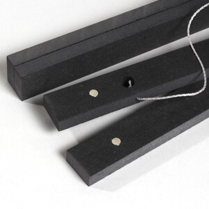 May include: Three black wooden rods with a string connecting them. Each rod has a small silver magnet on the top.
