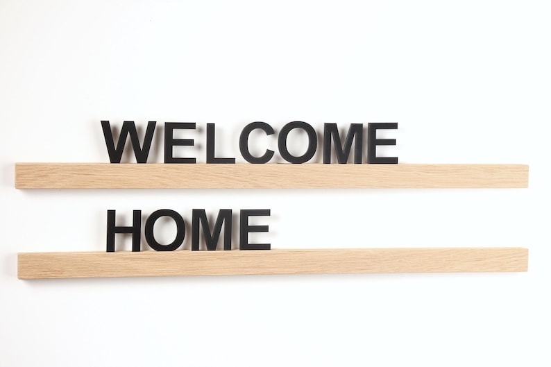 Puede incluir: Dos estantes de madera con las palabras "WELCOME" y "HOME" en letras negras.