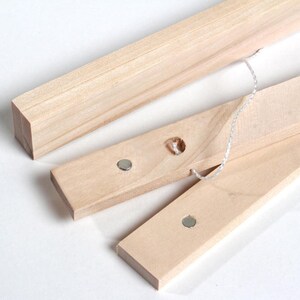 May include: Three wooden picture frame bars with metal magnets and a white string attached. The bars are made of natural wood and have a smooth finish.