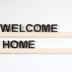 Puede incluir: Dos estantes de madera con las palabras "WELCOME" y "HOME" en letras negras.