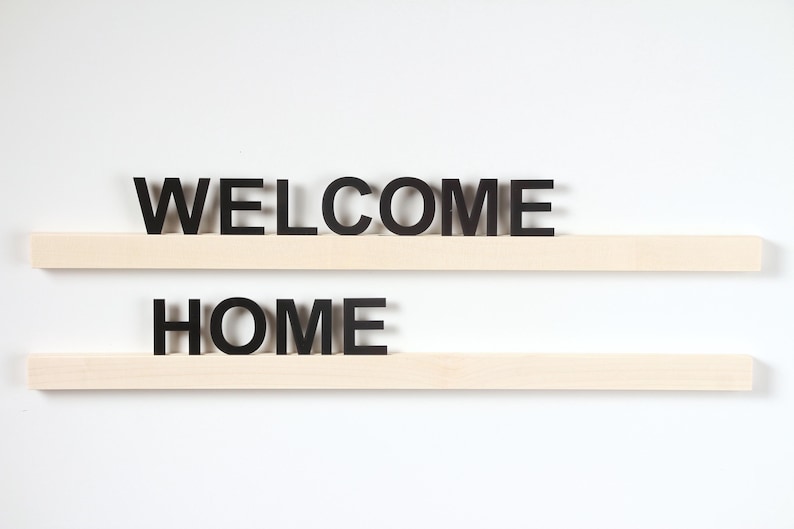 Puede incluir: Dos estantes de madera con las palabras "WELCOME" y "HOME" en letras negras.