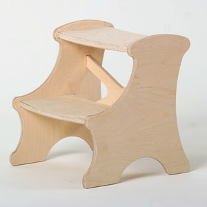 Peut inclure: Un tabouret en bois naturel à deux marches. La marche supérieure est légèrement plus large que la marche inférieure. Le tabouret a un design arrondi et incurvé.