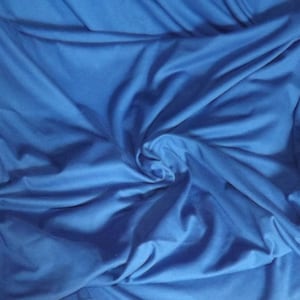 May include: A close-up shot of a vibrant blue fabric with soft folds and subtle shadows. The material appears to be smooth and flowing, with a slight sheen, suggesting a luxurious texture. The fabric is gathered in a spiral pattern.