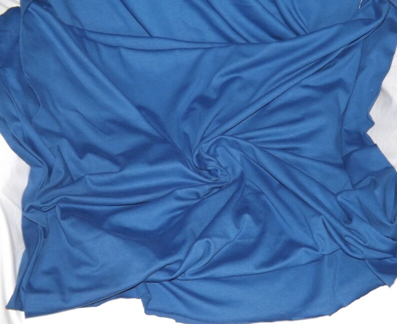 May include: A close-up shot of a deep blue fabric with soft folds and a subtle sheen. The fabric is draped over a white surface, creating a contrast. The texture appears smooth and flowing, suggesting a lightweight material.