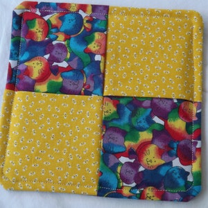 May include: A yellow and purple quilted hot pad with a cat print. The hot pad is made of four squares, two of which are yellow with white polka dots and two of which are purple with rainbow cats.