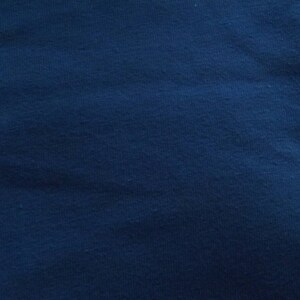 May include: A close-up shot of a textured, navy blue fabric. The fabric has a slightly uneven surface, with subtle variations in color and texture. The overall appearance is a deep, solid blue.