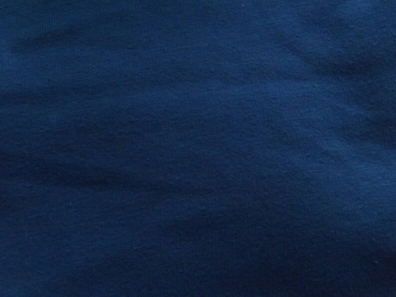 May include: A close-up shot of a textured, navy blue fabric. The fabric has a slightly uneven surface, with subtle variations in color and texture. The overall appearance is a deep, solid blue.