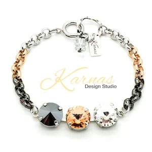 May include: A silver, black, and rose gold chain bracelet with three crystal stones. The stones are black, light orange, and clear. The bracelet has a lobster clasp and a charm that says "Karmas Design Studio".