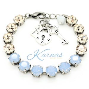 May include: A silver bracelet with a light blue and champagne crystal design. The bracelet features a charm with a padlock and key.