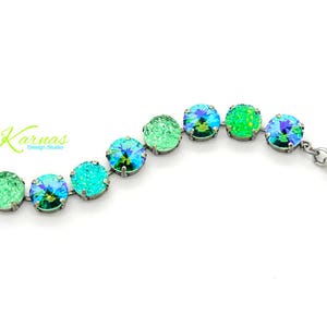 May include: A silver chain bracelet with a series of round, iridescent green and blue crystals. The bracelet has a silver clasp and a small silver charm with the word "Karmas" on it.
