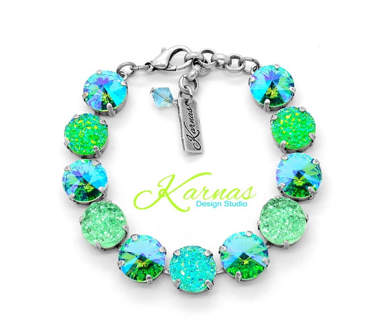 May include: A silver bracelet with alternating green and blue crystal beads. The bracelet has a silver clasp and a small tag with the text "Karnas Design Studio".