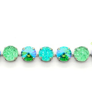 May include: A close-up of a silver chain with alternating green and blue crystal rhinestones. The rhinestones have a faceted, iridescent finish.