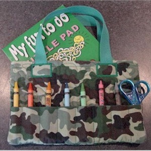 May include: A camouflage-patterned tote bag with a teal handle and pockets holding colorful crayons and a pair of blue scissors. A green notepad with the text "My fun to do" is inside the bag.
