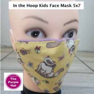 May include: A yellow face mask with a purple trim and a pattern of cats and butterflies. The mask is on a mannequin head. The text "In the Hoop Kids Face Mask 5x7" is at the top of the image. The text "The Purple Hat" is in a circle at the bottom of the image.