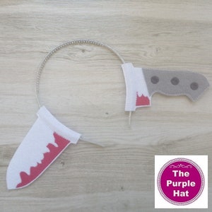 May include: A white headband with two felt knife shapes attached. The knife shapes are white with red painted on them to look like blood. The headband is silver and sparkly. The text "The Purple Hat" is visible in the lower right corner of the image.