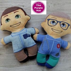 May include: Two plush dolls, one wearing a blue shirt with a truck on the pocket and brown pants, the other wearing a blue shirt with a stethoscope and a red cross on the pocket and green pants.