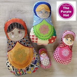 May include: Four colorful, handmade Matryoshka dolls with embroidered faces and floral aprons. The dolls are in various sizes, with the largest featuring an orange head covering and the smallest a pink gingham pattern. The Purple Hat logo is in the upper right corner.