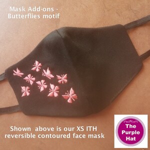May include: Black face mask with pink butterfly embroidery. The mask is reversible and contoured. The text "Mask Add-ons - Butterflies motif" is at the top of the image. The text "Shown above is our XS ITH reversible contoured face mask" is at the bottom of the image. The text "The Purple Hat" is in a purple circle at the bottom right of the image.