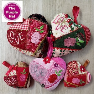 Può includere: Una collezione di cinque ornamenti in tessuto a forma di cuore. Ogni ornamento presenta un design patchwork con dettagli ricamati, tra cui la parola «LOVE» e motivi floreali. La tavolozza dei colori include rosso, rosa e bianco, con nastri per appenderli.