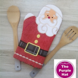 May include: Red and white Santa Claus oven mitt with a black belt and yellow buttons. The mitt is on a wooden surface with two wooden spoons.