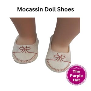 May include: A pair of off-white felt moccasin doll shoes featuring decorative dark red stitching in a bow pattern on the toe and a stitched border along the edge. The text "Mocassin Doll Shoes" and a purple circular logo with "The Purple Hat" are visible.