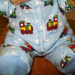 Pode incluir: Pijama azul claro com pés com um padrão repetido de comboios de brinquedo coloridos e estrelas brancas. O pijama tem um fecho frontal e é feito de um material macio e felpudo. O pijama foi concebido para uma criança.